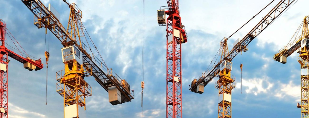 Several large construction cranes with yellow and red metal frames stand against a cloudy sky.